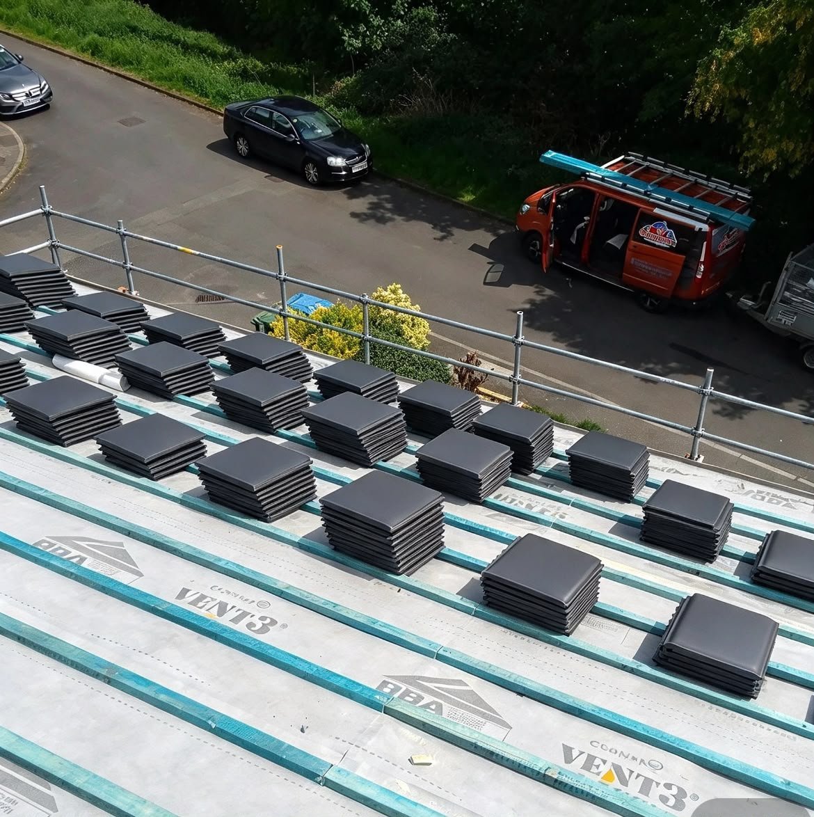 Aerial view of a residential roof with solar panels installed, cars parked on street below
